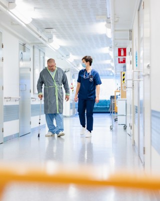 Potilas ja sairaanhoitaja kävelevät osaston käytävällä